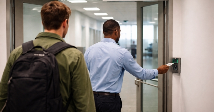 Employee holding door open at secure facility entrance demonstrating tailgating security risk where unauthorized person follows through access point
